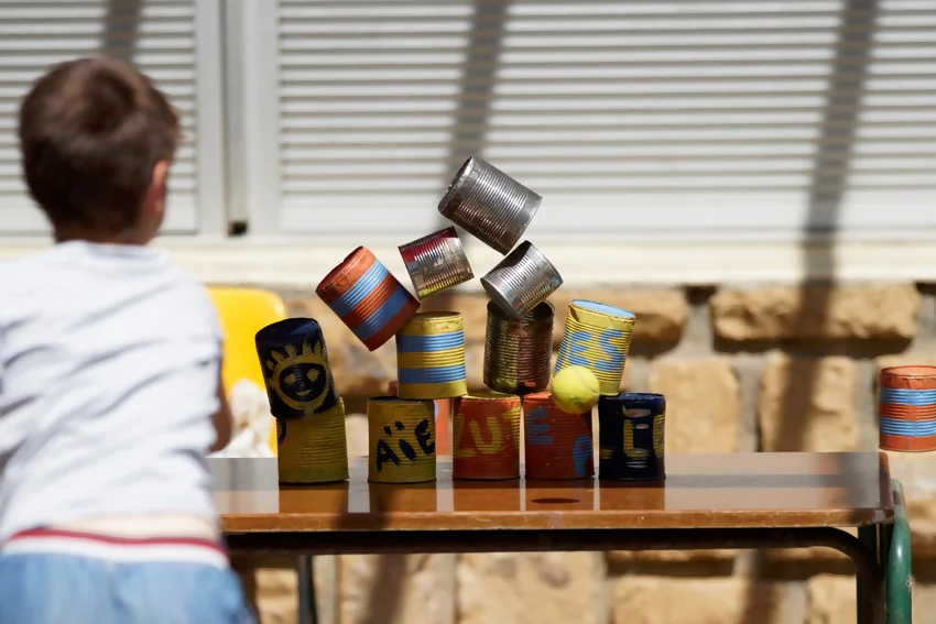 un enfant lance des balles dans une pile de boites de conserve à une kermesse d'école